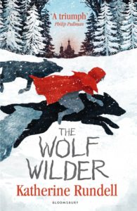 Book cover
Text: 'A triumph' Philip Pullman
The Wolf Wilder
Katherine Rundell
Bloomsbury
Image: Illustration of a girl in a red coat riding a black wolf on a snowy landscape