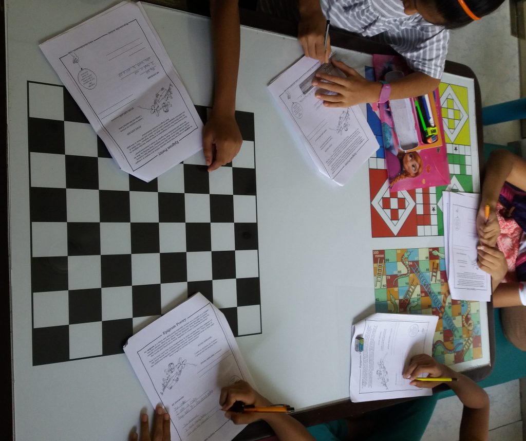 Five children (no faces) working on a poetry exercise at a colourful games table