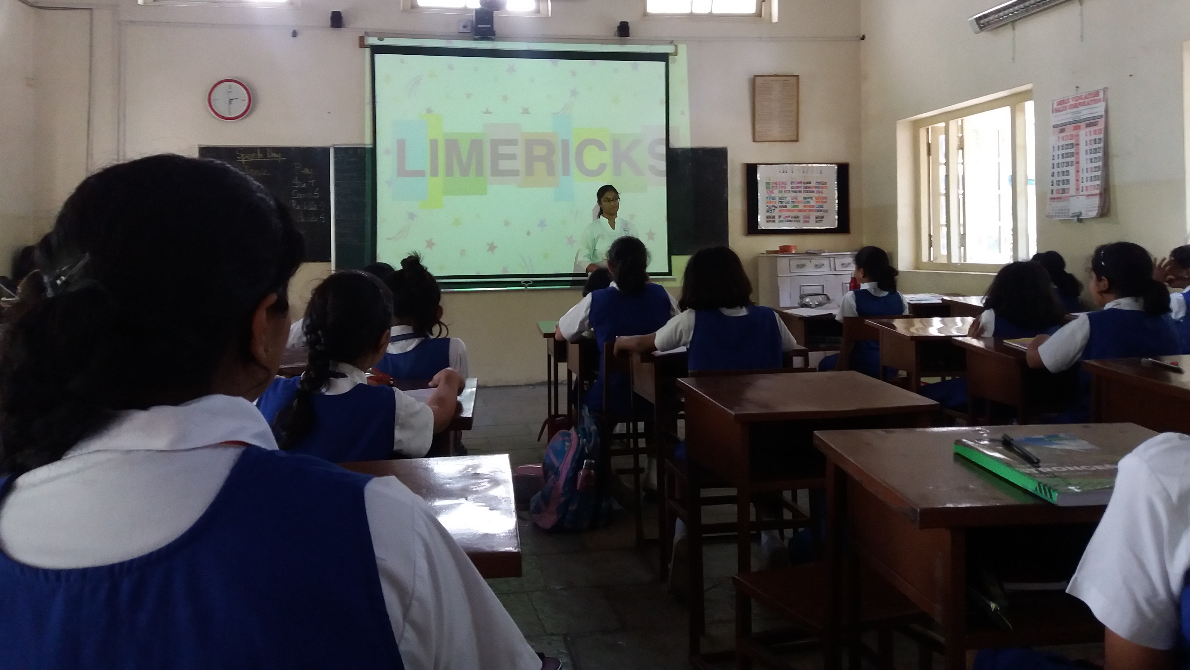 Audio-visual display that says 'Limericks'
A student standing before it, talking to a class of girls (no faces visible)