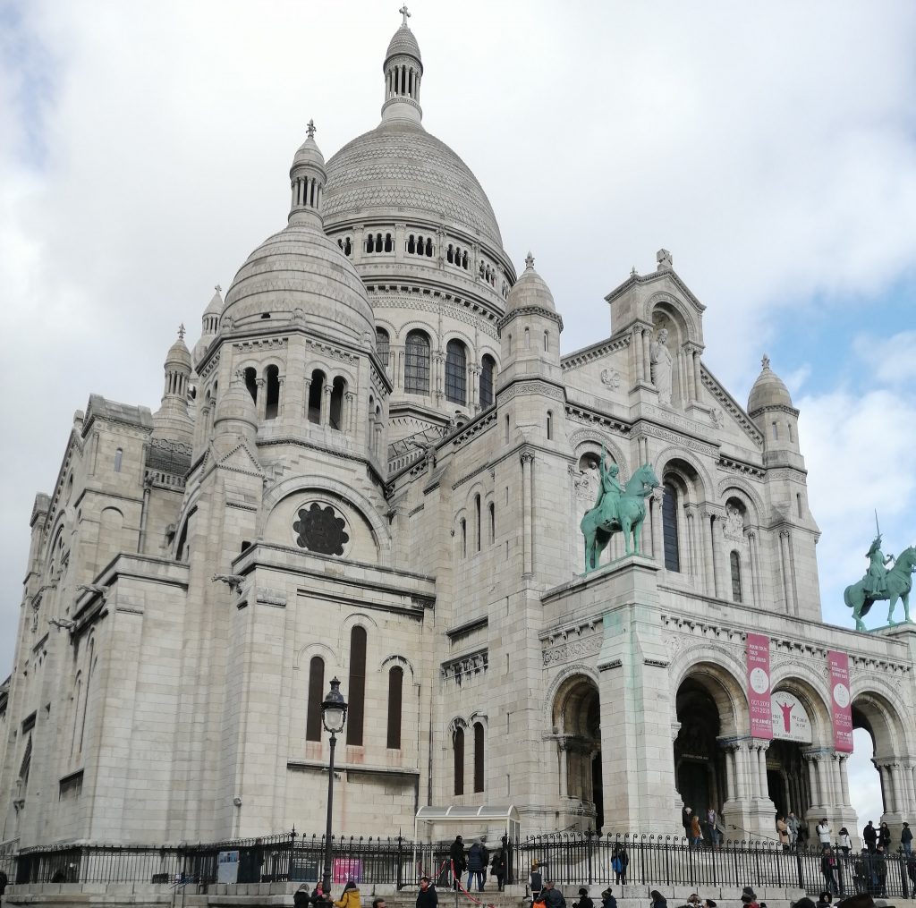 The Sacre Coeur - a white domed cathedral with two green statues of people horseback close to the entrance