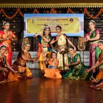 Dancers in Bharatanatyam costume in a semi-circle. In the centre, one dancer dressed as Krishna