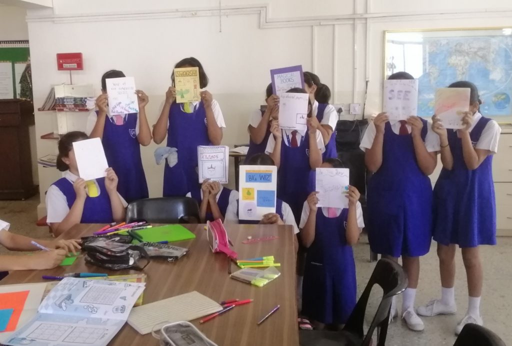 Ten girls in school uniform hiding their faces behind handmade magazines