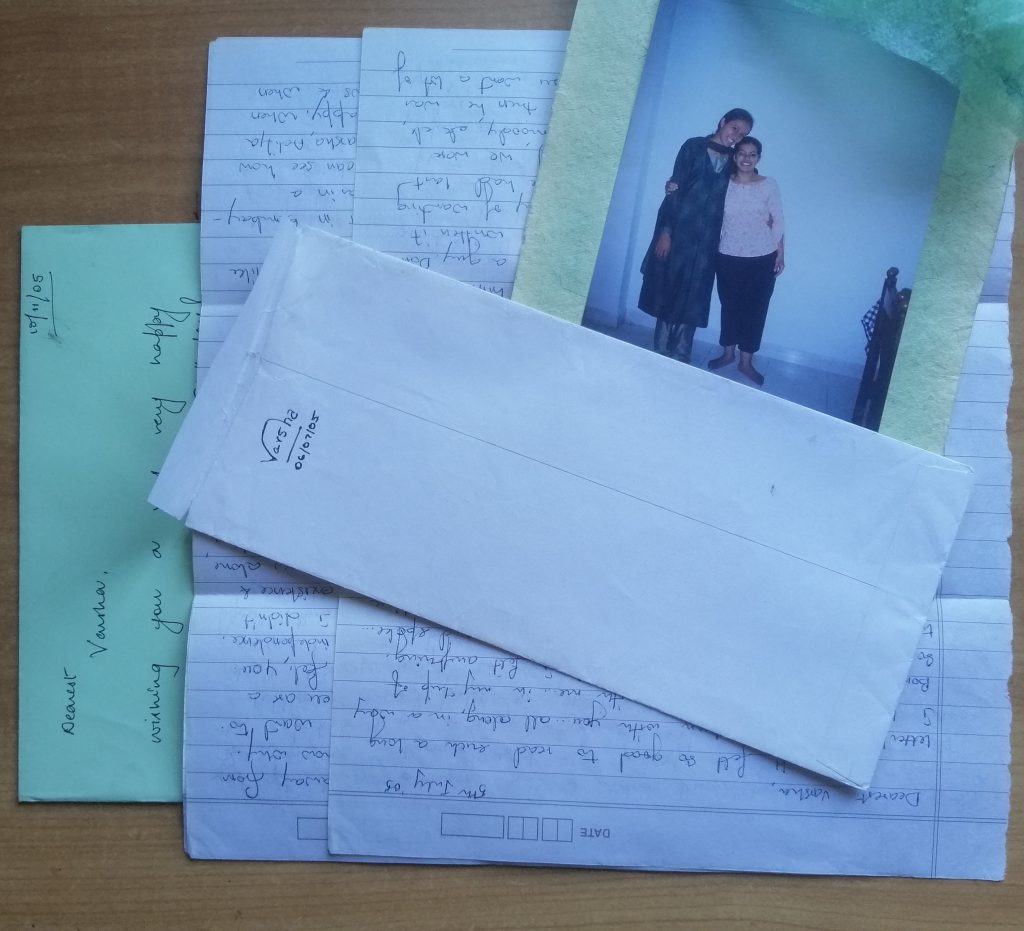 A pile of letters partially covered by a photograph of two girls and an envelop signed Varsha 06/07/05